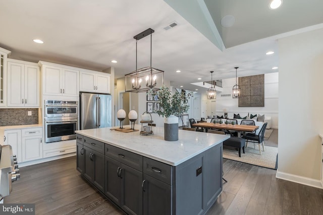 kitchen featuring appliances with stainless steel finishes, dark wood-type flooring, hanging light fixtures, and white cabinetry