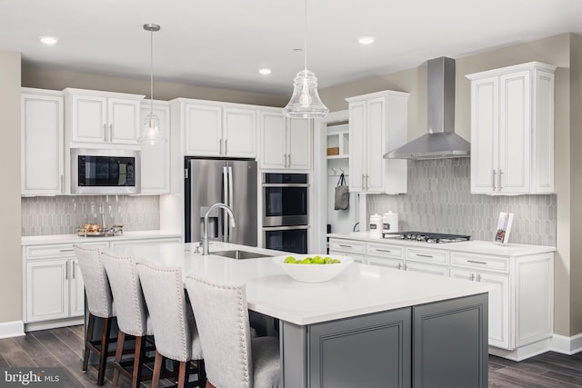 kitchen featuring a center island with sink, backsplash, wall chimney exhaust hood, and stainless steel appliances