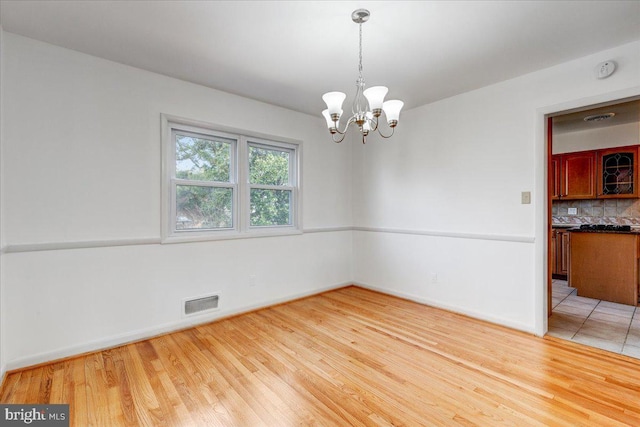 unfurnished room featuring a chandelier and light wood-type flooring