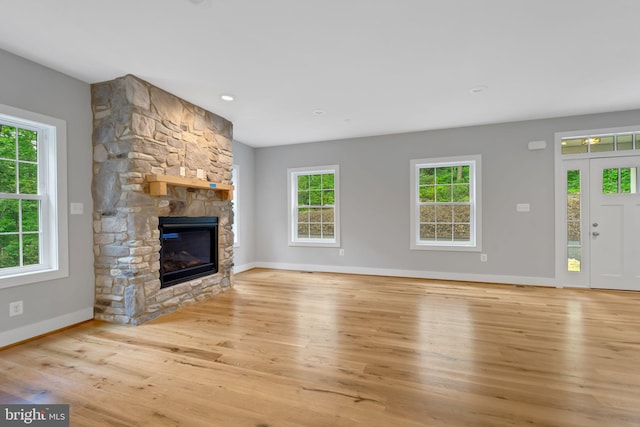 unfurnished living room with a stone fireplace, a healthy amount of sunlight, and light wood-type flooring