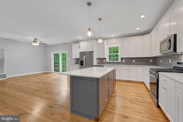 kitchen with appliances with stainless steel finishes, pendant lighting, white cabinetry, sink, and a center island