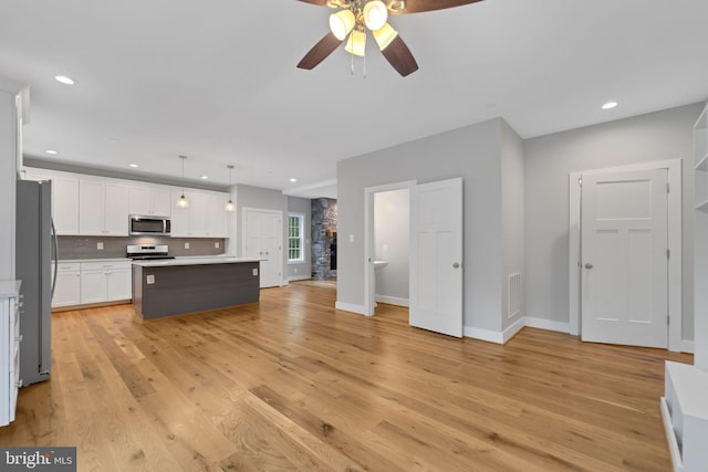 kitchen featuring white cabinetry, decorative light fixtures, a center island, light wood-type flooring, and appliances with stainless steel finishes