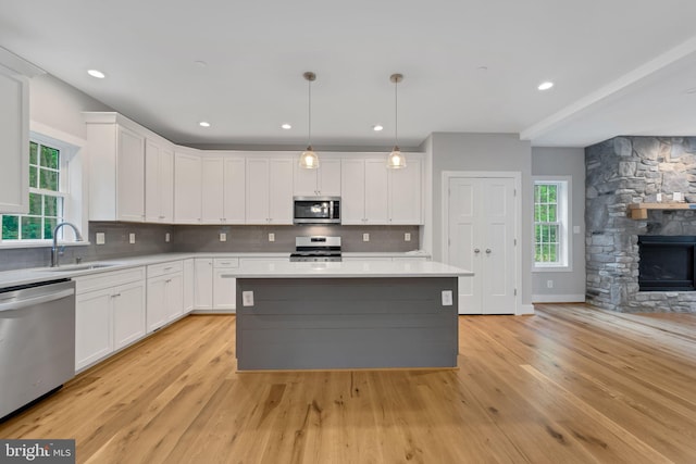 kitchen featuring appliances with stainless steel finishes, white cabinetry, hanging light fixtures, a center island, and tasteful backsplash