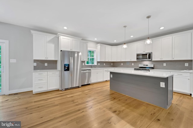 kitchen featuring sink, white cabinetry, hanging light fixtures, light hardwood / wood-style flooring, and stainless steel appliances