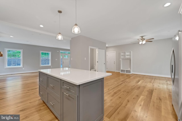 kitchen with gray cabinets, stainless steel refrigerator, decorative light fixtures, a center island, and light hardwood / wood-style flooring