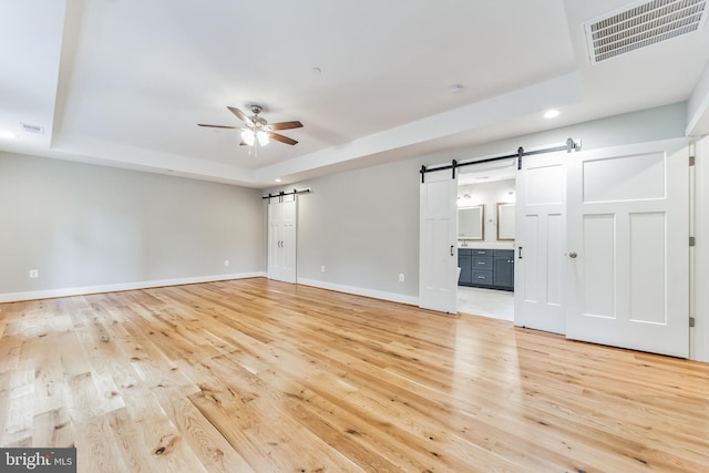 unfurnished living room with a tray ceiling, light hardwood / wood-style floors, and a barn door