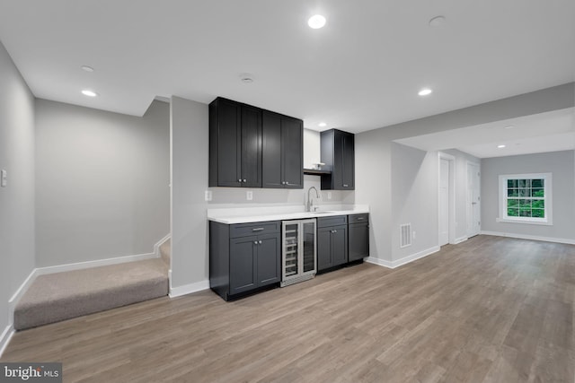 bar with wine cooler, sink, and light wood-type flooring