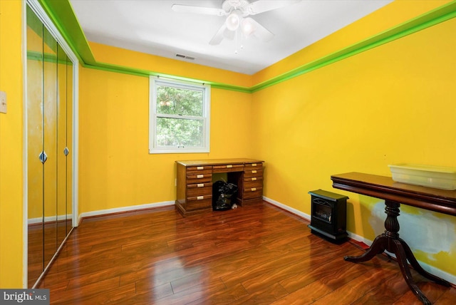 home office featuring wood-type flooring, ceiling fan, and a wood stove