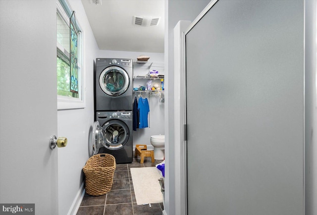 laundry room with stacked washer and clothes dryer and dark tile floors