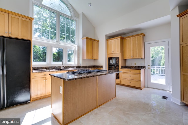 kitchen with a center island, dark stone countertops, black appliances, sink, and light tile floors