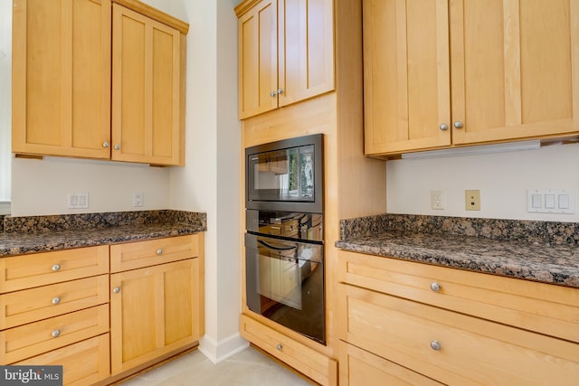 kitchen with light brown cabinets, dark stone countertops, black appliances, and light tile flooring