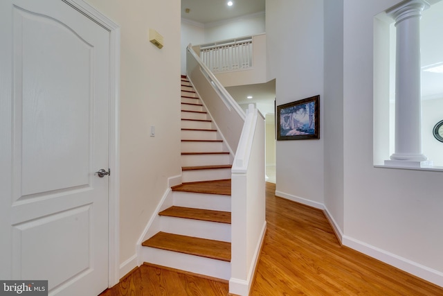 stairway featuring light hardwood / wood-style flooring, crown molding, and ornate columns