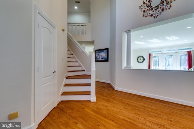 stairs with light hardwood / wood-style floors and decorative columns