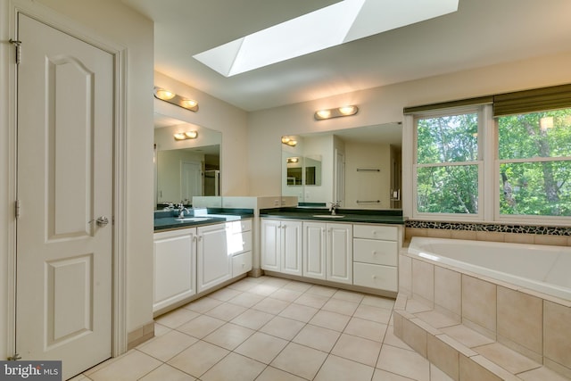 bathroom with dual bowl vanity, tile flooring, tiled tub, and a skylight