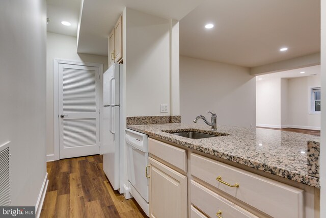 kitchen with white appliances, sink, light stone countertops, and hardwood / wood-style flooring