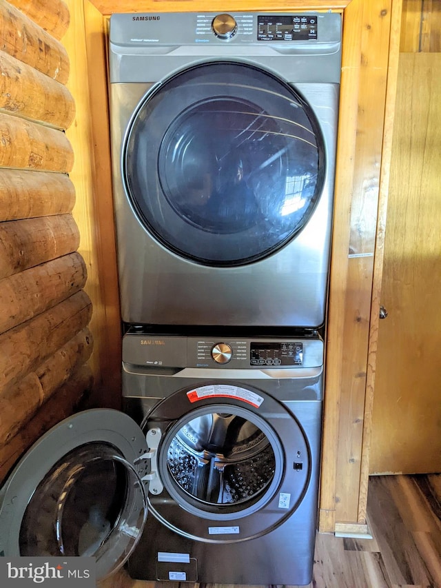 clothes washing area featuring log walls, wood-type flooring, and stacked washing maching and dryer