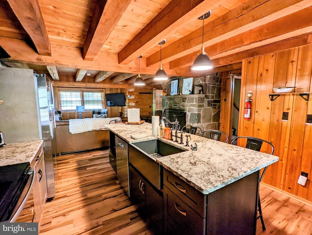 kitchen featuring a stone fireplace, light hardwood / wood-style flooring, wooden walls, beamed ceiling, and a kitchen breakfast bar