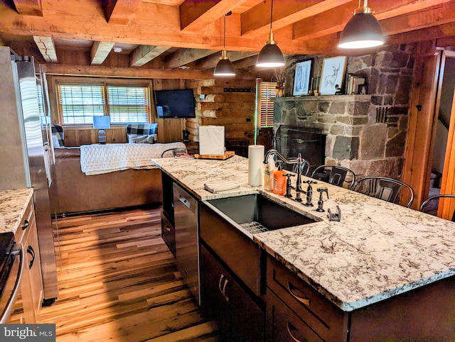 kitchen with beamed ceiling, a fireplace, sink, light hardwood / wood-style floors, and hanging light fixtures