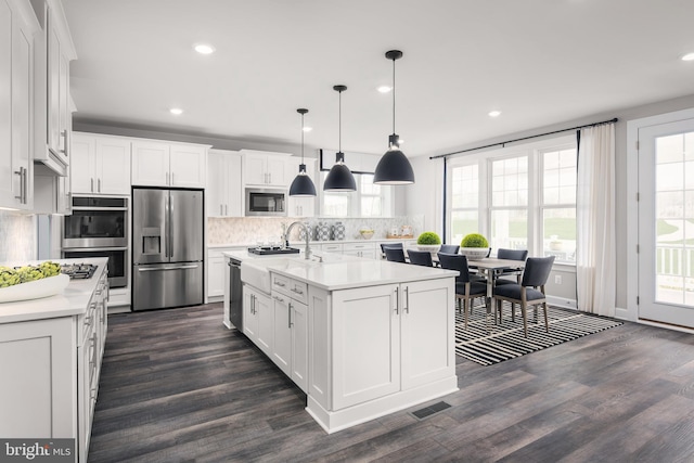 kitchen featuring white cabinetry, hanging light fixtures, stainless steel appliances, dark wood-type flooring, and a kitchen island with sink