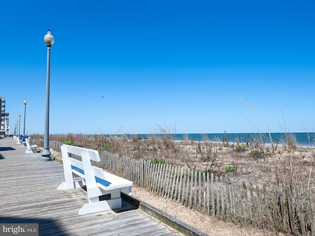 deck with a water view, fence, and a beach view