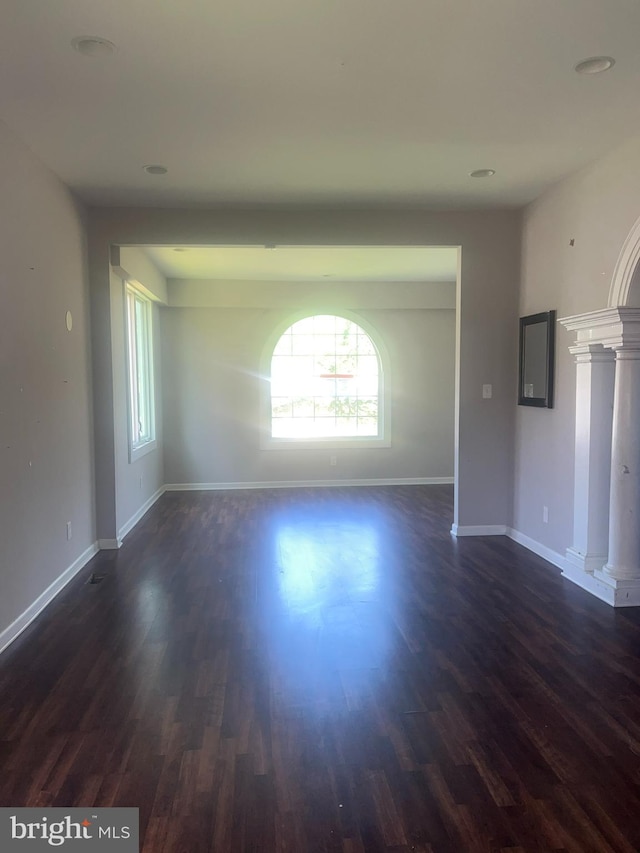 spare room featuring ornate columns, a wealth of natural light, and dark hardwood / wood-style flooring