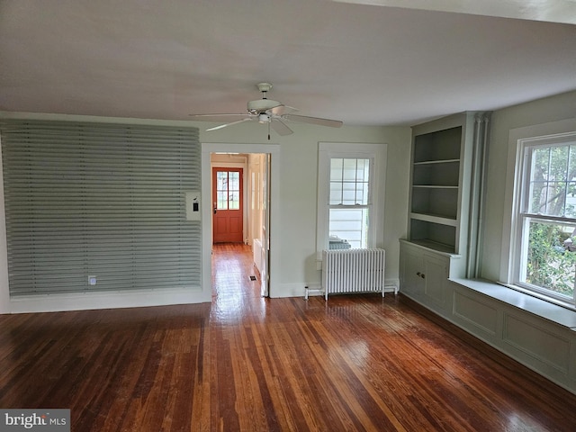 empty room featuring built in features, dark hardwood / wood-style flooring, radiator heating unit, and ceiling fan