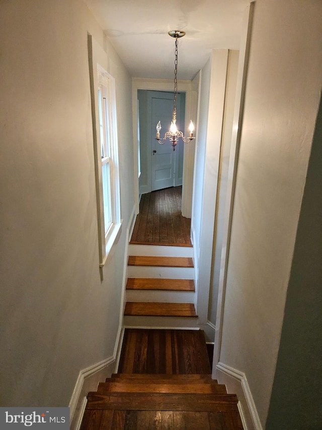 stairs with dark wood-type flooring and a chandelier