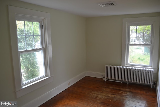 empty room featuring dark hardwood / wood-style flooring, radiator heating unit, and a wealth of natural light