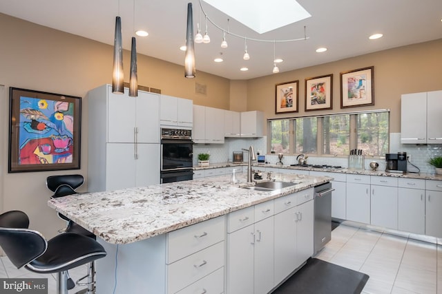 kitchen with sink, a skylight, backsplash, white cabinetry, and a center island with sink