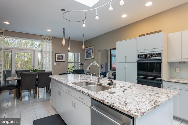 kitchen featuring white cabinets, a center island with sink, dishwasher, black double oven, and sink