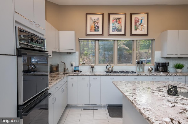 kitchen featuring light stone countertops, sink, white cabinetry, decorative backsplash, and black double oven