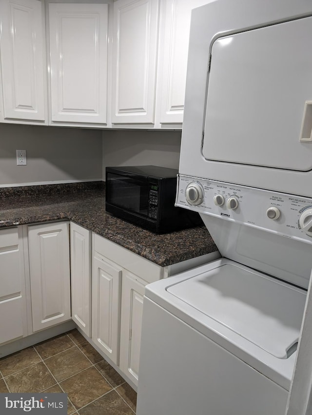 laundry room featuring dark tile floors and stacked washing maching and dryer