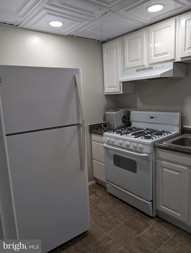 kitchen with white cabinets, white appliances, dark tile floors, and wall chimney exhaust hood