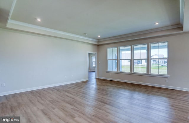 spare room featuring a raised ceiling, crown molding, and light hardwood / wood-style flooring