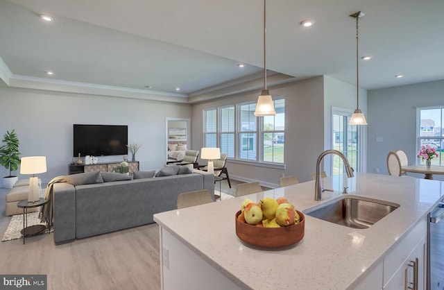 kitchen with light stone counters, sink, light hardwood / wood-style floors, hanging light fixtures, and an island with sink