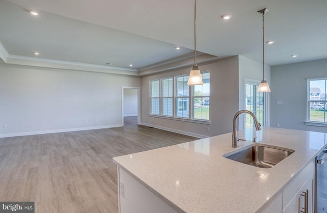 kitchen featuring light stone countertops, light hardwood / wood-style flooring, decorative light fixtures, a center island with sink, and white cabinets