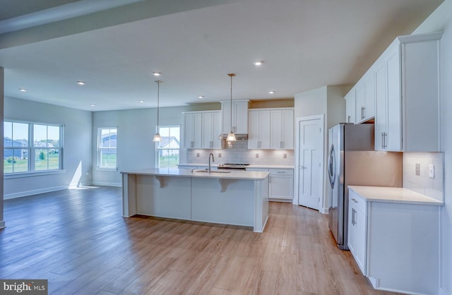 kitchen with decorative backsplash, light hardwood / wood-style floors, white cabinetry, hanging light fixtures, and an island with sink