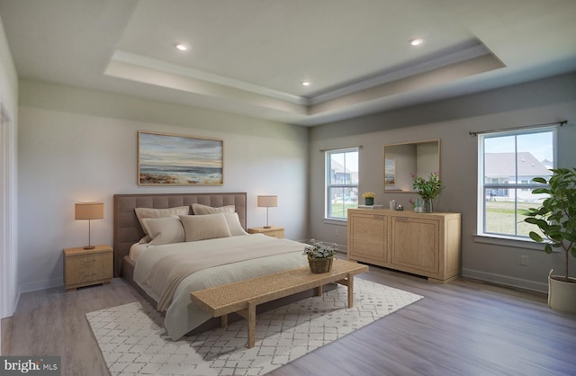 bedroom featuring a tray ceiling, multiple windows, and light hardwood / wood-style flooring