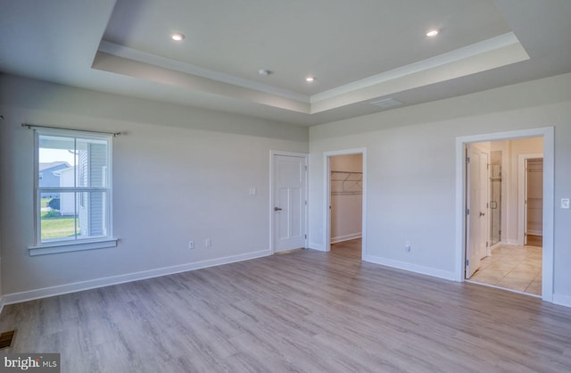 unfurnished bedroom featuring a raised ceiling, light hardwood / wood-style flooring, a spacious closet, connected bathroom, and a closet