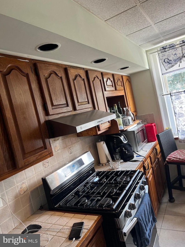 kitchen featuring a drop ceiling, range with gas stovetop, light tile patterned flooring, and backsplash