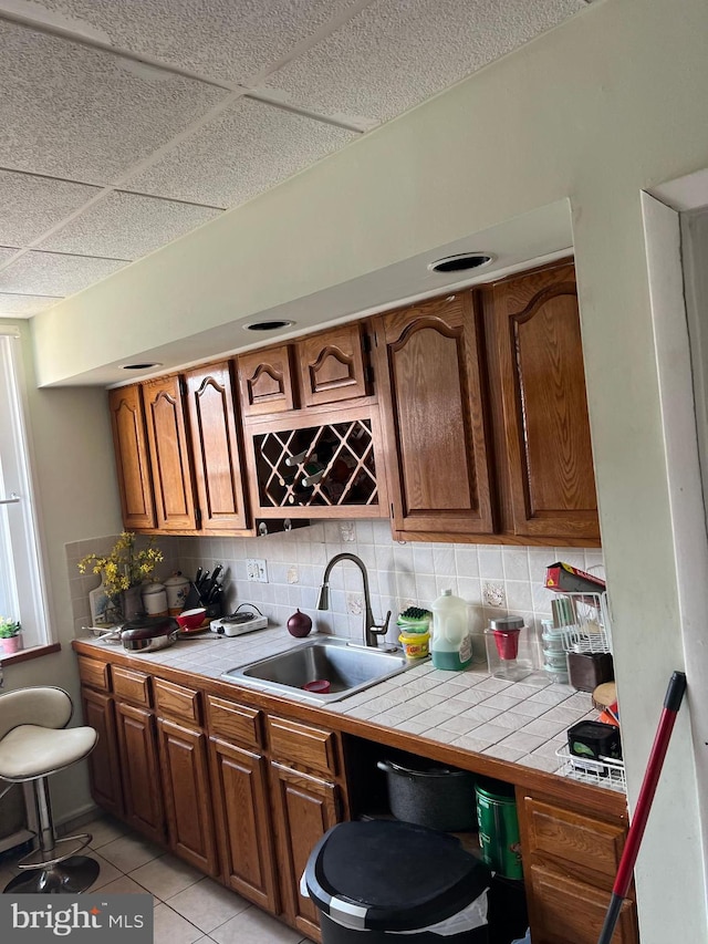 kitchen featuring a drop ceiling, light tile patterned floors, decorative backsplash, tile countertops, and sink