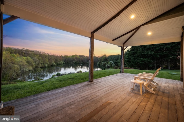 deck at dusk featuring a lawn and a water view