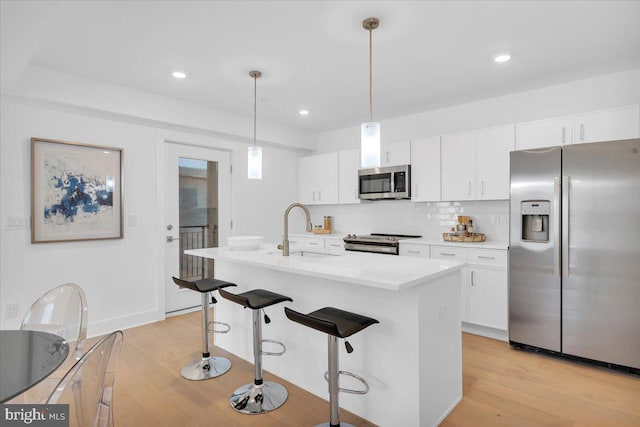 kitchen featuring stainless steel appliances, a kitchen island with sink, decorative light fixtures, light hardwood / wood-style flooring, and white cabinets