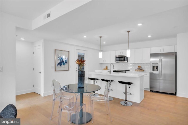 kitchen featuring a kitchen breakfast bar, hanging light fixtures, light hardwood / wood-style flooring, appliances with stainless steel finishes, and white cabinetry