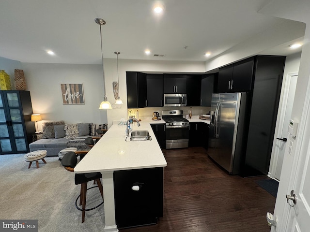 kitchen featuring dark cabinetry, a peninsula, a sink, light countertops, and appliances with stainless steel finishes