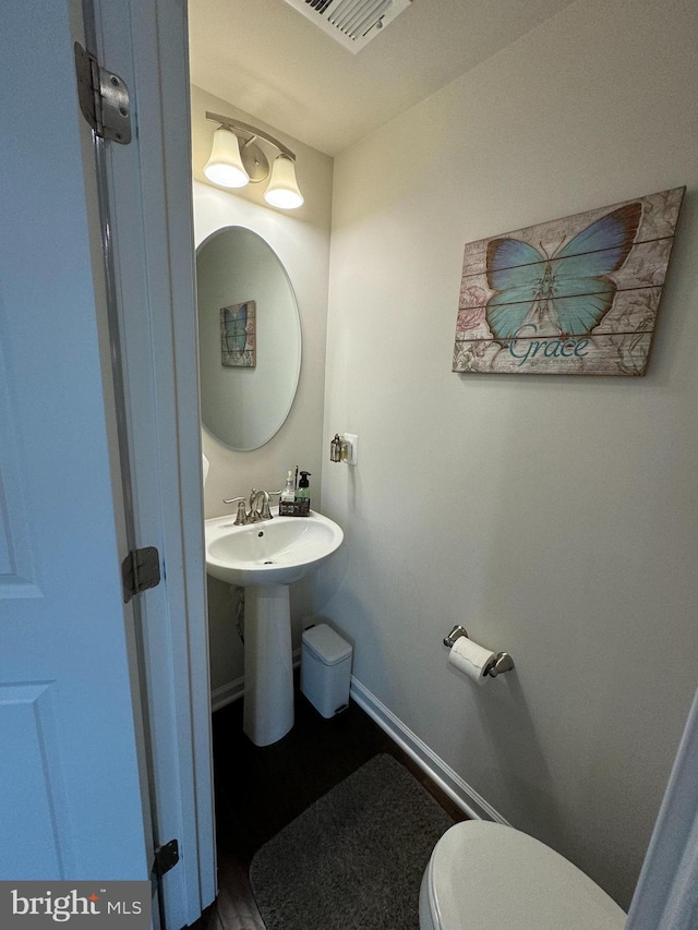 half bath featuring a sink, visible vents, baseboards, and toilet