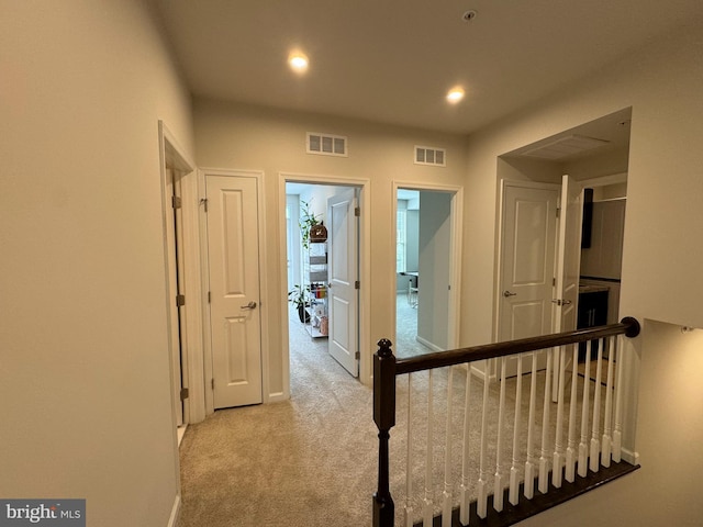 hallway with recessed lighting, visible vents, carpet floors, and an upstairs landing