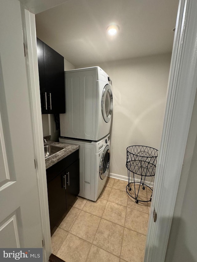 laundry area with stacked washer and clothes dryer, a sink, cabinet space, light tile patterned flooring, and baseboards