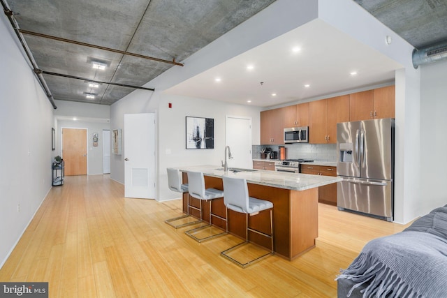 kitchen featuring a kitchen bar, backsplash, light hardwood / wood-style flooring, a center island with sink, and stainless steel appliances