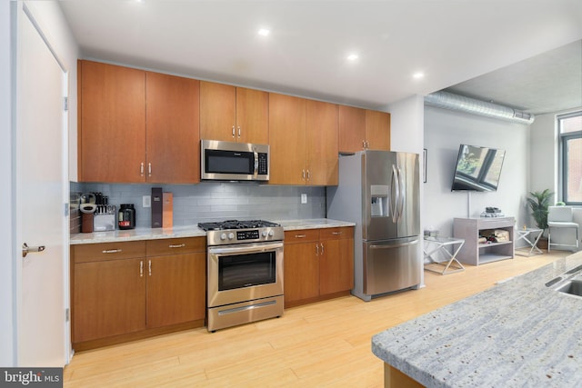 kitchen with appliances with stainless steel finishes, light wood-type flooring, backsplash, and light stone counters